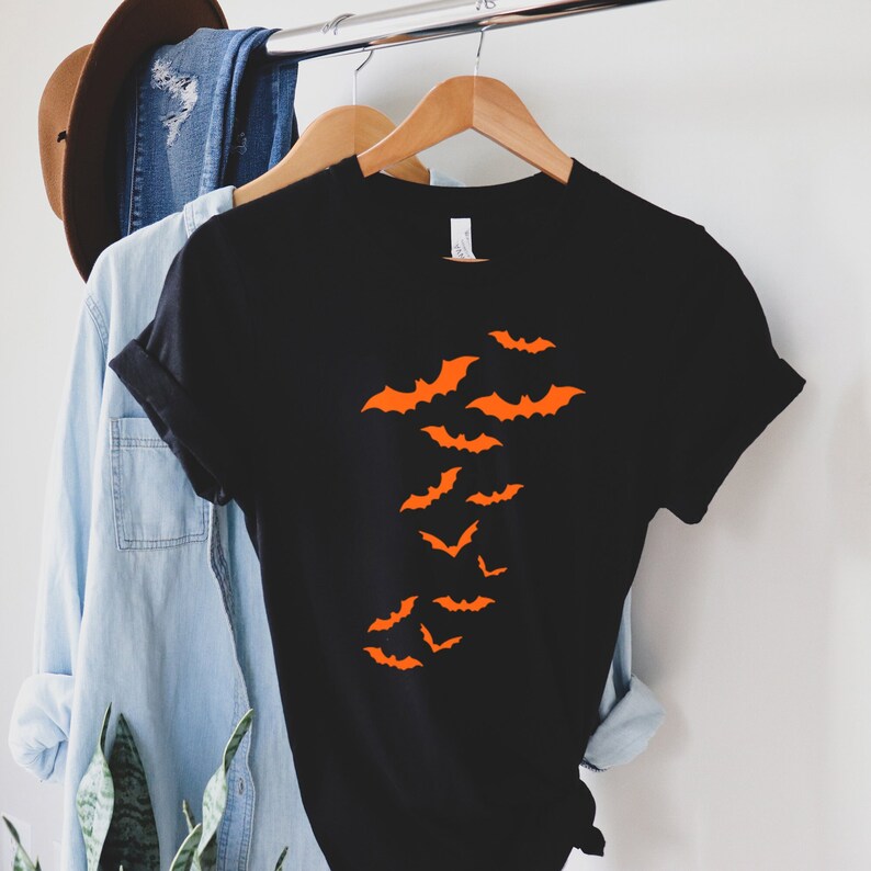 Puede incluir: Camiseta negra con un dise&ntilde;o de murci&eacute;lagos naranjas volando en un grupo.