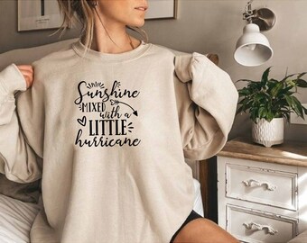 May include: A beige sweatshirt with black text that reads "Sunshine mixed with a little hurricane".