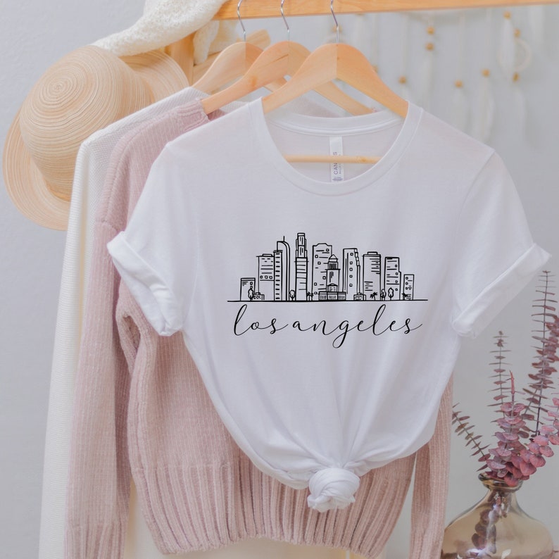 Peut inclure: T-shirt blanc avec un graphique noir de l'horizon de Los Angeles et le texte "los angeles" en dessous.
