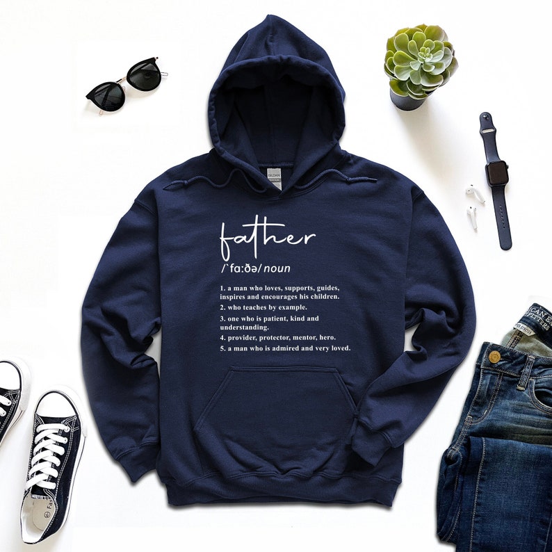 K&ouml;nnte beinhalten: Marineblauer Kapuzenpullover mit dem Wort "father" in wei&szlig;er Schrift. Darunter befindet sich eine Definition von "father" in wei&szlig;em Text. Der Kapuzenpullover hat eine Vordertasche und eine Kapuze mit Kordelzug. Der Kapuzenpullover liegt auf einer wei&szlig;en Oberfl&auml;che.