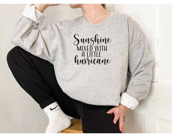 May include: A gray sweatshirt with the text "Sunshine mixed with a little hurricane" printed in black.