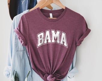 May include: A maroon t-shirt with the word "BAMA" printed in white on the front. The shirt is tied in a knot at the bottom.