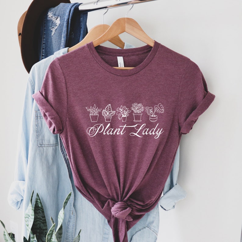 K&ouml;nnte beinhalten: Ein maroonfarbenes T-Shirt mit einer wei&szlig;en Grafik von Topfpflanzen und dem Text "Plant Lady".