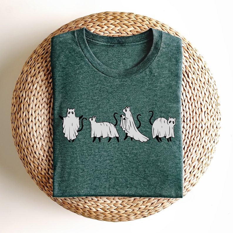 May include: A dark green t-shirt with a graphic of five cats dressed as ghosts. The cats are in a line, facing forward, and each has a white ghost sheet draped over their body. The graphic is in black and white.