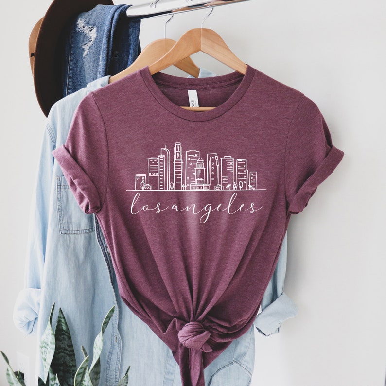 Peut inclure: Un t-shirt marron avec une silhouette blanche de l'horizon de Los Angeles et le texte "los angeles" en dessous.