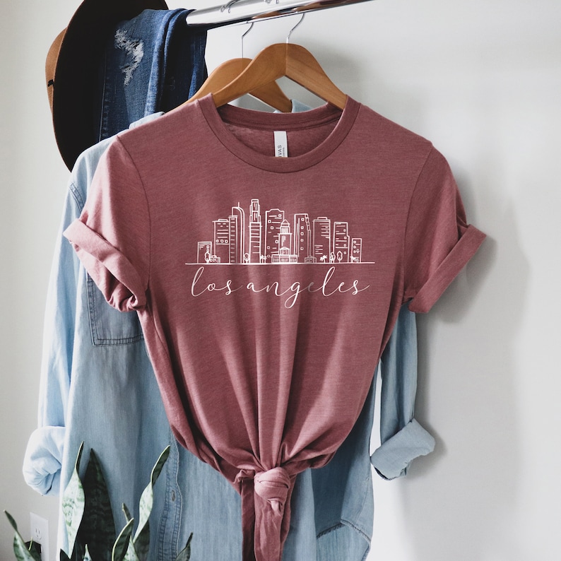 Peut inclure: Un t-shirt marron avec un graphique blanc de l'horizon de Los Angeles et le texte "los angeles" en &eacute;criture cursive.