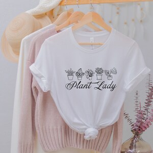 K&ouml;nnte beinhalten: Wei&szlig;es T-Shirt mit einer schwarzen Grafik von Topfpflanzen und dem Text "Plant Lady".
