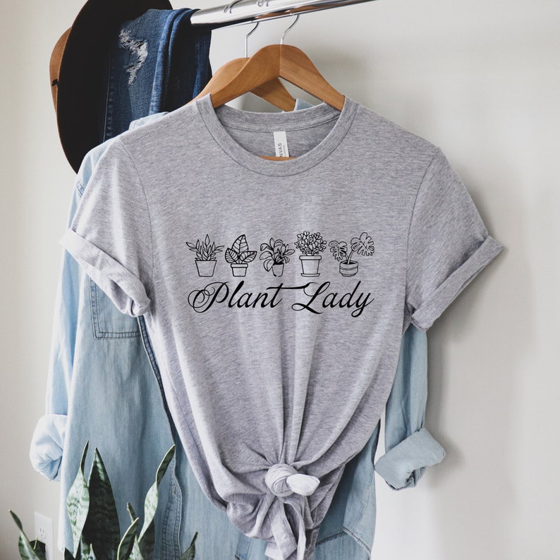 K&ouml;nnte beinhalten: Graues T-Shirt mit kurzen &Auml;rmeln und einem schwarzen Aufdruck von Topfpflanzen und dem Text "Plant Lady".