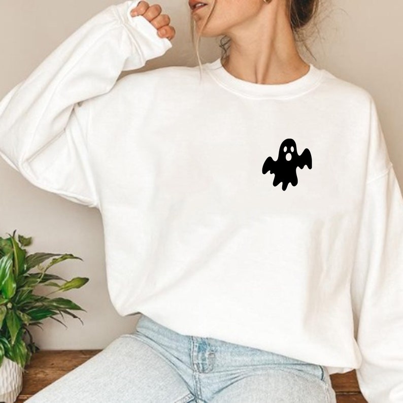 May include: White sweatshirt with a black ghost graphic on the front. The ghost has a surprised expression and is wearing a simple, rounded shape.