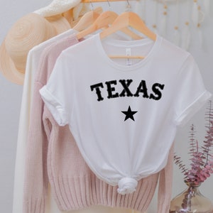 May include: White t-shirt with black text that says "TEXAS" and a black star.