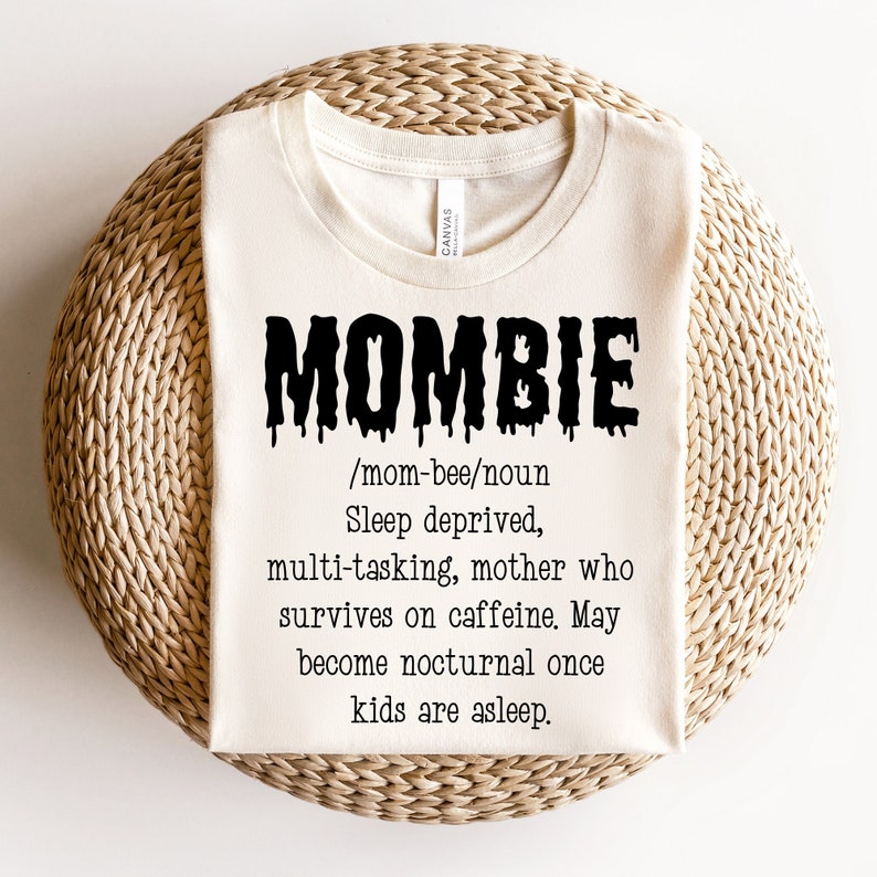 May include: A white t-shirt with black text that reads "MOMBIE /mom-bee/noun Sleep deprived, multi-tasking, mother who survives on caffeine. May become nocturnal once kids are asleep."