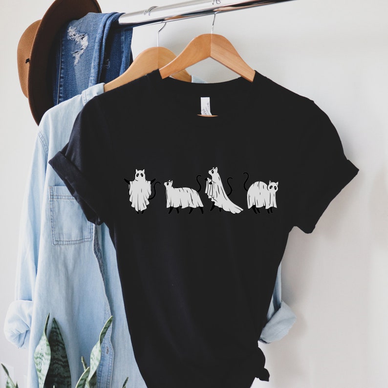 May include: Black t-shirt with a graphic of five cats dressed as ghosts. The cats are in a line, facing forward, and each has a different pose. The graphic is in white and is centered on the shirt.