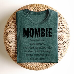 May include: A dark green t-shirt with a black graphic that says "MOMBIE /mom-bee/noun Sleep deprived, multi-tasking, mother who survives on caffeine. May become nocturnal once kids are asleep."