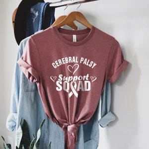 May include: A maroon t-shirt with the text "Cerebral Palsy Support Squad" in white with a white ribbon and hearts.