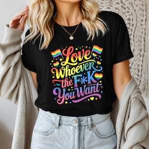 May include: Black t-shirt with a colorful graphic that reads "Love Whoever the F*K You Want." The design includes rainbow flags, hearts, and stars. The shirt is a crew neck style.