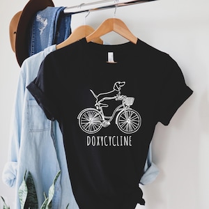 Camiseta con juego de palabras sobre doxiciclina en farmacias, perro salchicha en bicicleta, camiseta de farmacéutico, regalo para amantes de los perros, regalo de farmacia, camiseta de perro salchicha, camiseta para amantes de los perros
