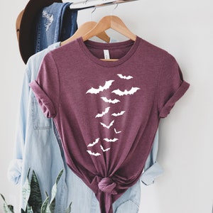 Puede incluir: Una camiseta color granate con un gr&aacute;fico blanco de murci&eacute;lagos volando en l&iacute;nea vertical. La camiseta est&aacute; colgada en una percha.