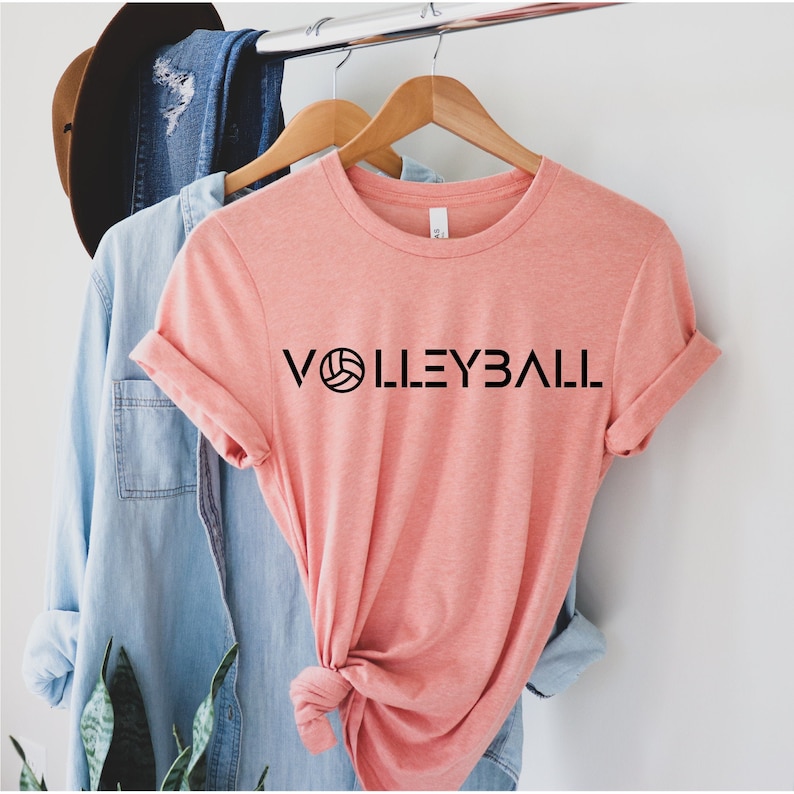 May include: A pink t-shirt with the word "VOLLEYBALL" printed in black with a volleyball graphic.