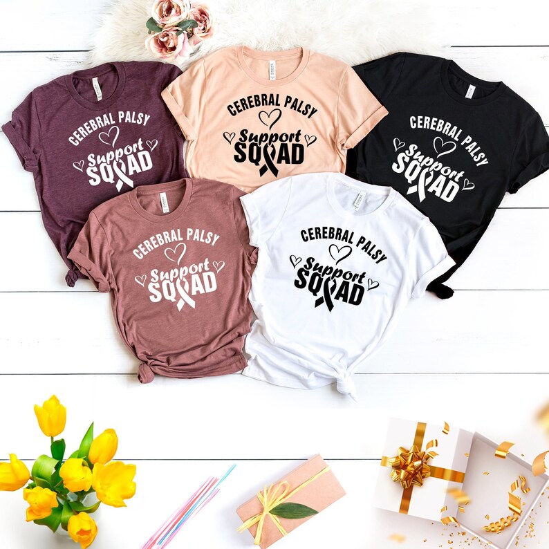 May include: Five t-shirts in different colors with the text "Cerebral Palsy Support Squad" and a black ribbon with a heart on each shirt.
