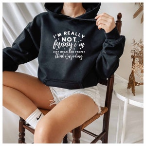 May include: A black cropped hoodie with white text that reads "I'm really not funny, I'm just mean and people think I'm joking".