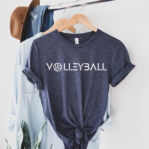May include: A navy blue t-shirt with a white graphic of a volleyball and the word "VOLLEYBALL" in white letters.