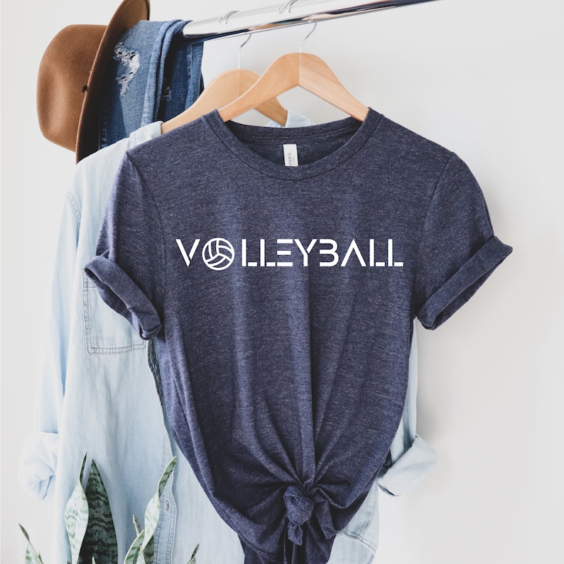 May include: A navy blue t-shirt with a white graphic of a volleyball and the word "VOLLEYBALL" in white letters.