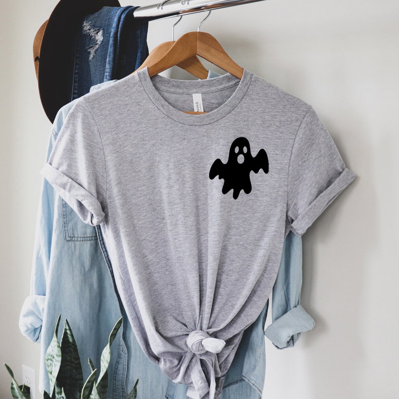 以下が含まれることがあります： 前面に黒い幽霊のグラフィックがプリントされたグレーのTシャツ。幽霊は驚いた表情をして、白いシーツを着ています。