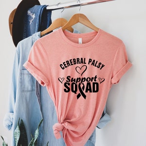 May include: A pink t-shirt with the text "Cerebral Palsy Support Squad" in black lettering. The text is surrounded by small hearts and a black ribbon.