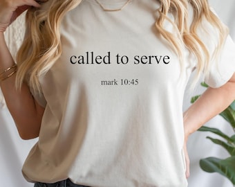 Può includere: T-shirt color crema con la scritta "called to serve" e il riferimento "mark 10:45" stampati in nero. La maglietta è di uno stile semplice e casual.