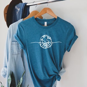 May include: A teal blue t-shirt with a white graphic of two hands holding a globe. The graphic is a simple line drawing.