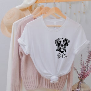 May include: White t-shirt with a black silhouette of a Labrador Retriever and the name "Bella" printed on the front.