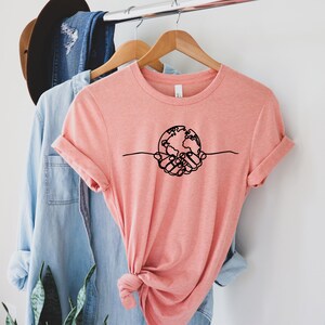 May include: A peach-coloured t-shirt with a black line drawing of two hands holding a globe.