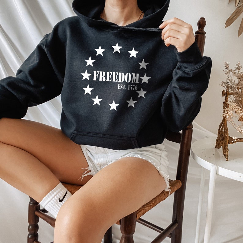 May include: Black cropped hoodie with a white graphic print of a circle of stars and the text "FREEDOM EST. 1776".