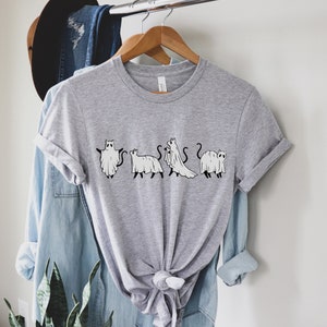 May include: Gray t-shirt with a graphic of five cats dressed as ghosts. The cats are in a line, facing forward, and each has a different pose. The graphic is in black and white.