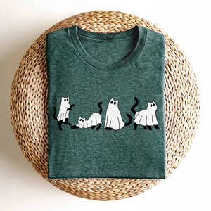 May include: A dark green t-shirt with a white graphic of five cats dressed as ghosts. The cats are in a line, with the first cat looking to the left, the second cat looking to the right, the third cat looking to the left, the fourth cat looking to the right, and the fifth cat looking to the left.