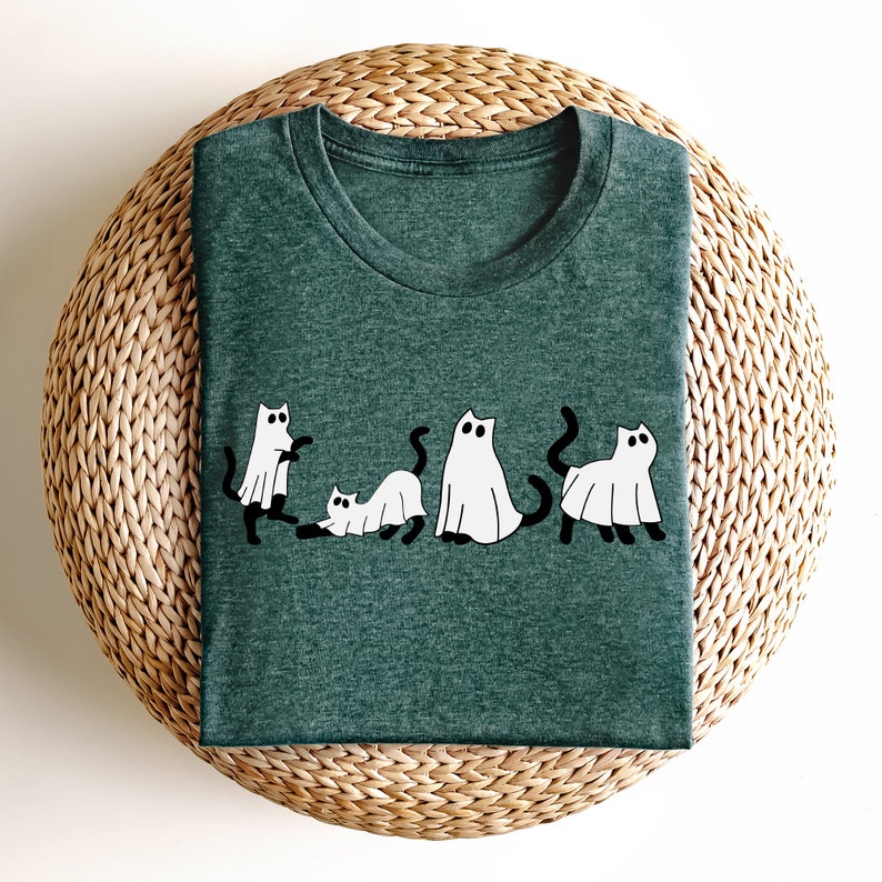 May include: A dark green t-shirt with a white graphic of five cats dressed as ghosts. The cats are in a line, with the first cat looking to the left, the second cat looking to the right, the third cat looking to the left, the fourth cat looking to the right, and the fifth cat looking to the left.