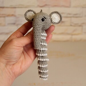 May include: A gray crocheted elephant keychain with white accents. The elephant has a long, curled trunk and large ears.