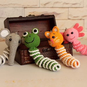 May include: Four crocheted animal keychains with colorful striped tails. The animals are an elephant, frog, cat, and axolotl.
