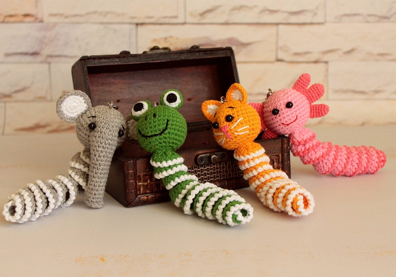 May include: Four crocheted animal keychains with colorful striped tails. The animals are an elephant, frog, cat, and axolotl.