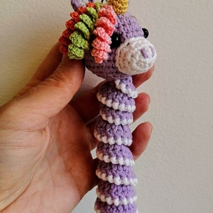 May include: A purple crocheted unicorn with a rainbow mane and a yellow horn. The unicorn is about 10 inches long and has a white crocheted tail.