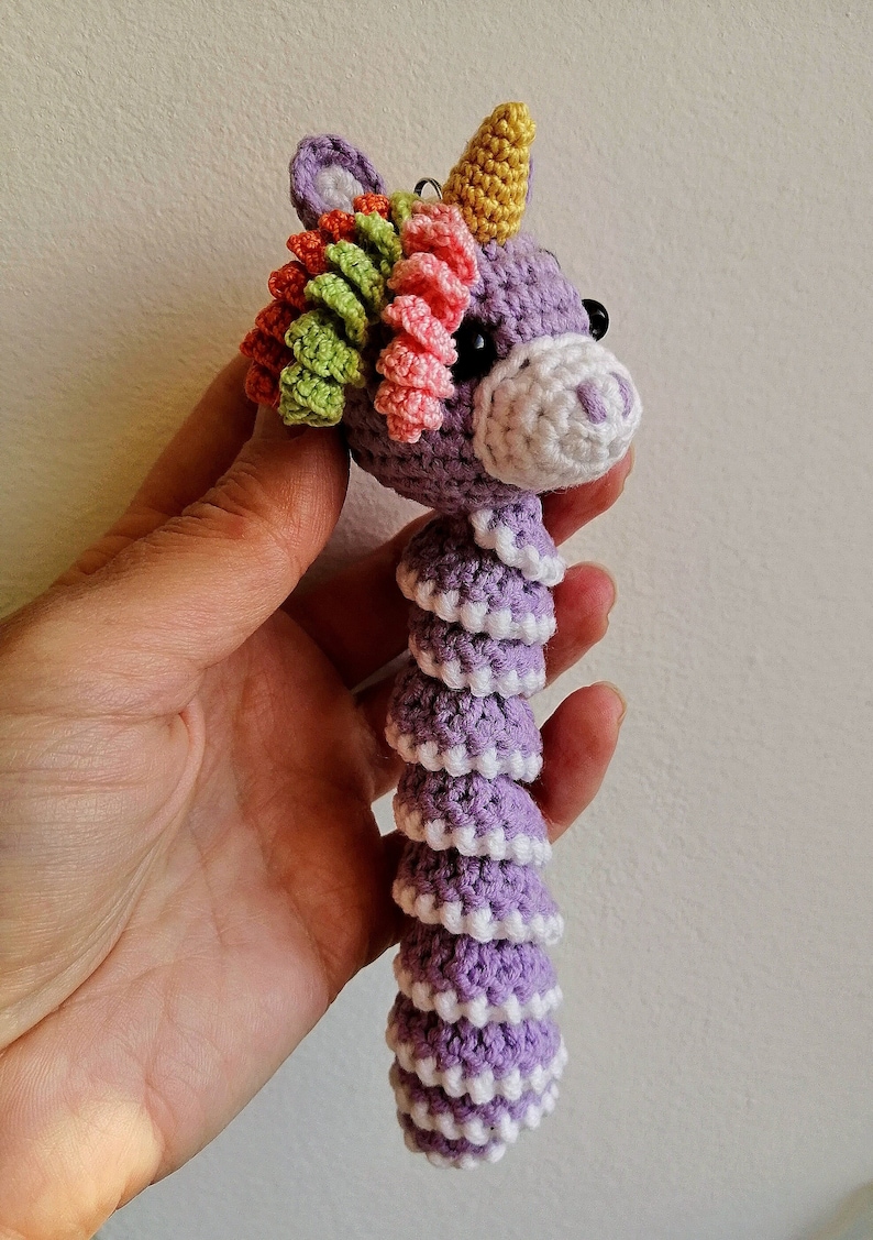 May include: A purple crocheted unicorn with a rainbow mane and a yellow horn. The unicorn is about 10 inches long and has a white crocheted tail.