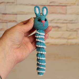 May include: A crocheted blue and white bunny keychain with a long, coiled tail. The bunny has a pink nose and black eyes.
