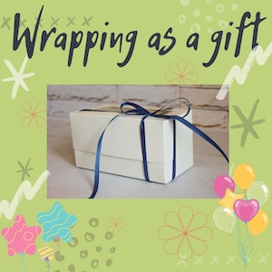 May include: A rectangular white gift box with a clear window on top, tied with a dark blue satin ribbon. The image features the text Wrapping as a gift in dark gray script, surrounded by a light green border with colorful balloon and star graphics.