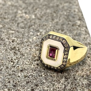 May include: A gold ring with a white enamel center and a pink gemstone. The ring is surrounded by small diamonds.
