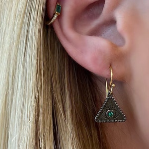 May include: Gold hoop earrings with a small green stone and a dangling triangle earring with a black eye and green stone.