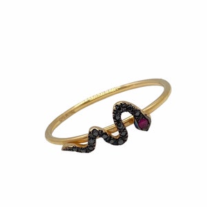 Könnte beinhalten: Ein goldener Ring mit einem Schlangendesign aus schwarzen Diamanten und einem roten Rubin als Auge.