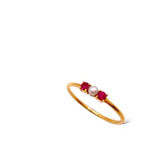 May include: A gold ring with three small stones. The stones are red and white.