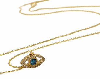 May include: A gold chain necklace with a small evil eye pendant. The pendant is made of gold and has a blue stone in the center. The stone is surrounded by smaller diamonds.