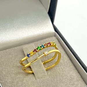 May include: A gold ring with a row of colorful gemstones and a single diamond in the center. The ring is in a black velvet ring box.