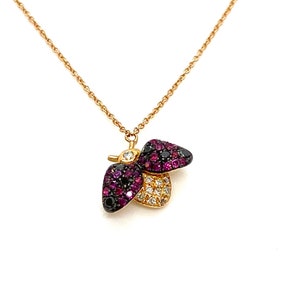 May include: A gold chain necklace with a bee pendant. The bee is made of gold and has black and pink gemstones.